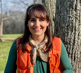 Woman in orange vest smiles in front of tree.