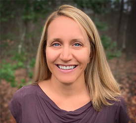 Woman smiles in wooded area.